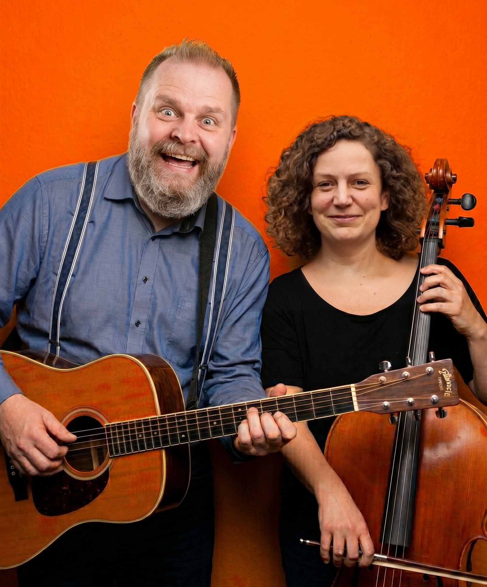 Knut Schfleck mit Gitarre und Claudia Herold mit Cello vor einer orangefarbenen Wand